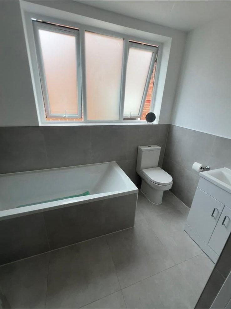 Finished bathroom with grey tiling, new bath, toilet and vanity unit